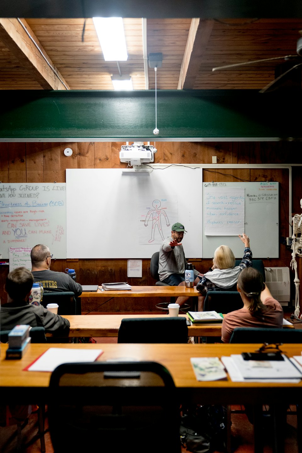 Instructor teaching adults about human anatomy at wooden desks.