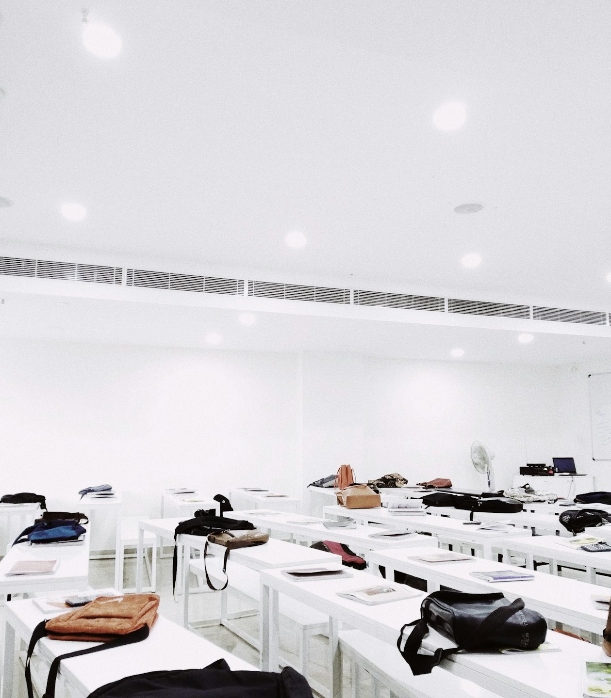 Empty modern classroom with rows of desks holding student belongings.