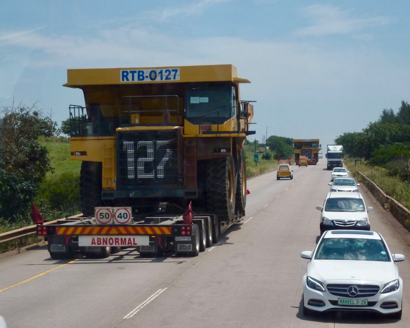 A massive yellow dump truck on a trailer travels down the highway.