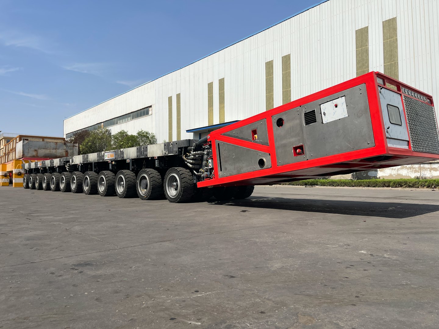A red modular heavy-haul trailer parked by an industrial building.